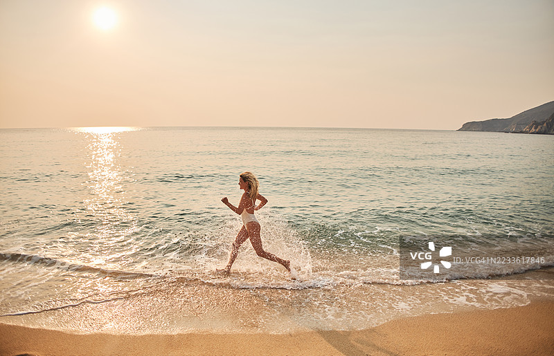 夕阳下，一位美丽的女子在海滩上奔跑在水中图片素材