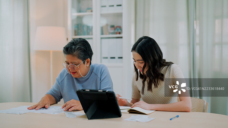 年轻的亚洲女性和年长的母亲在家中一起计算开支。图片素材
