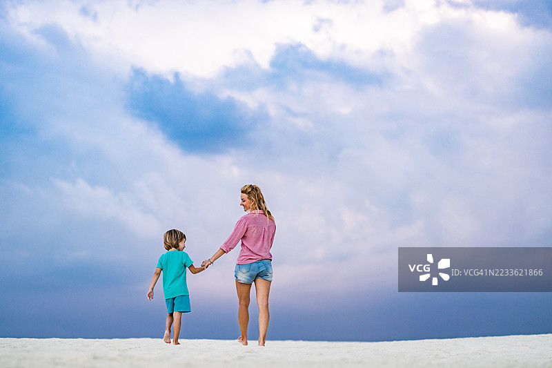 无忧无虑的单身母亲和儿子在海滩上散步的背影。图片素材