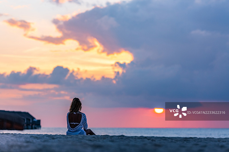 黄昏时分，一位女性在海滩上放松的背影。图片素材