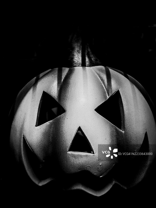 阴影中的发光微笑：经典的南瓜灯，三角形的眼睛和锯齿状的微笑照亮黑暗，通过光线、质感和节日的恐怖庆祝万圣节的迷人魅力图片素材