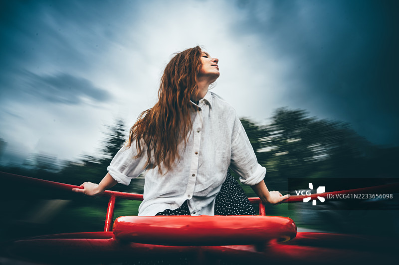一位红发女子张开双臂，在旋转木马上旋转。图片素材