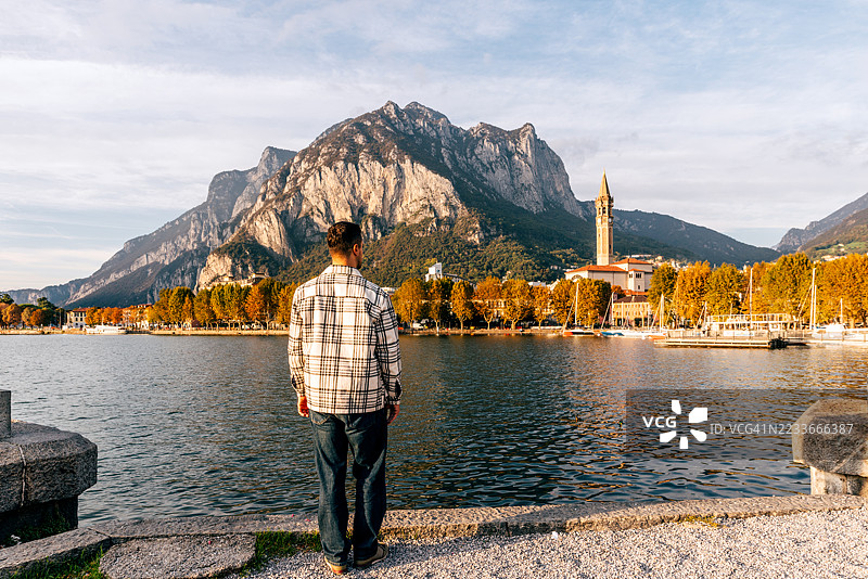 身穿格子衬衫的男子背影，俯瞰意大利伦巴第大区的莱科市景、科莫湖及周围山脉。图片素材
