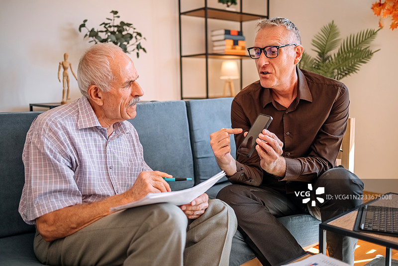 一名商人，从事金融行业，正在客户家中工作，使用数字平板电脑以便更好地解释如何投资储蓄。图片素材