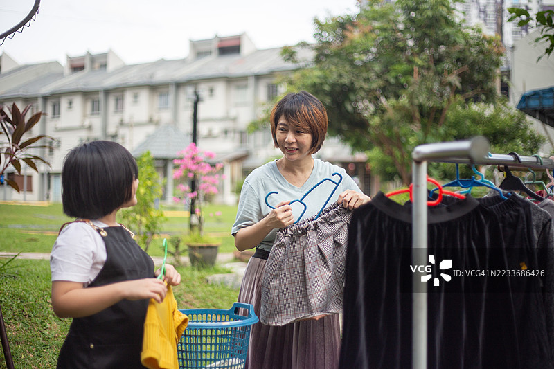 亚洲华裔母女在阳光明媚的日子里在花园里晾衣服。图片素材