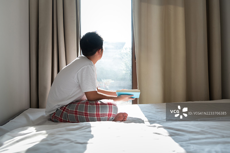 年轻的少年坐在床上阅读书籍图片素材