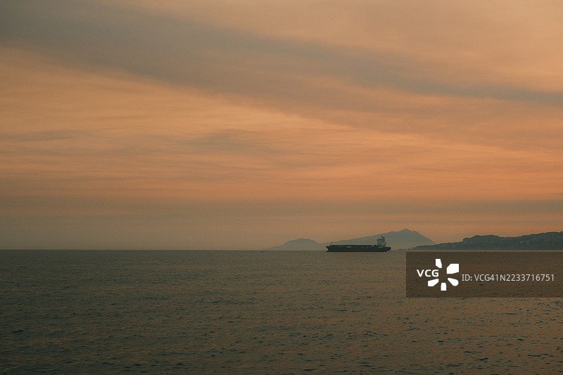 货船在日落时分航行，背景是山脉。图片素材