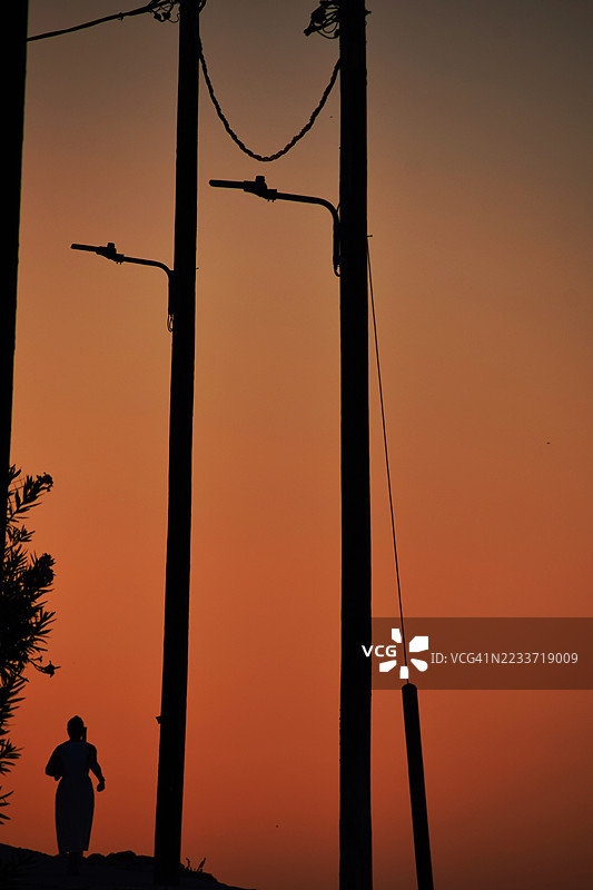一个人在街灯旁走动的剪影，背景是绚丽的日落天空，萨摩斯，希腊图片素材