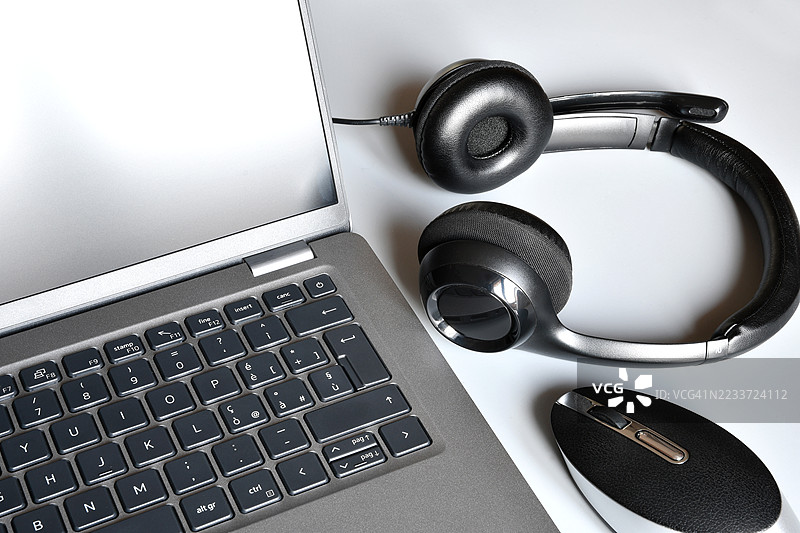 高角度视图的笔记本电脑、耳机和鼠标放在白色表面上图片素材