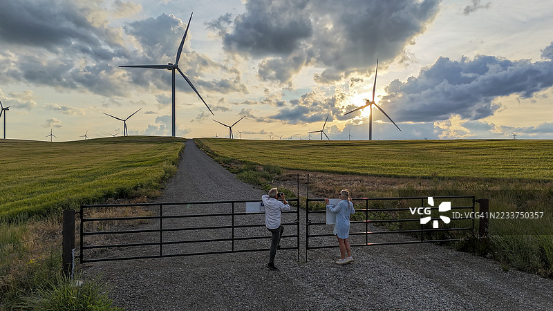 一对老年夫妇在风力涡轮机下的公路上拍照图片素材