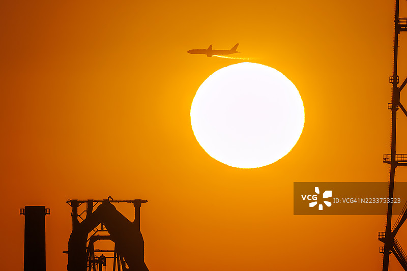 第一缕阳光与一架客机和鸟的剪影。它即将降落在附近的羽田机场。第一缕阳光从运河对岸的烟囱和电厂、钢铁厂上升。横滨,神奈川。图片素材