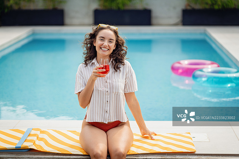女人在泳池旁放松，手里拿着饮料，脸上洋溢着快乐的表情图片素材