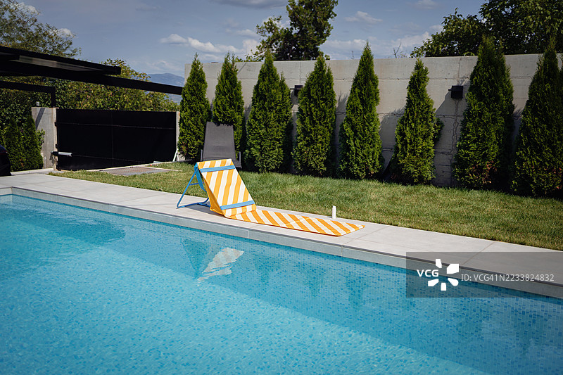 户外泳池边区域，配有躺椅和生机勃勃的绿色花园背景图片素材