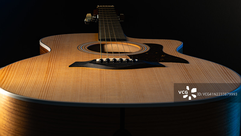 桌子上放着一把靠近的木吉他，背景为深色。图片素材