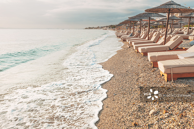 希腊日落时分的空旷海滩，配有躺椅和伞。图片素材
