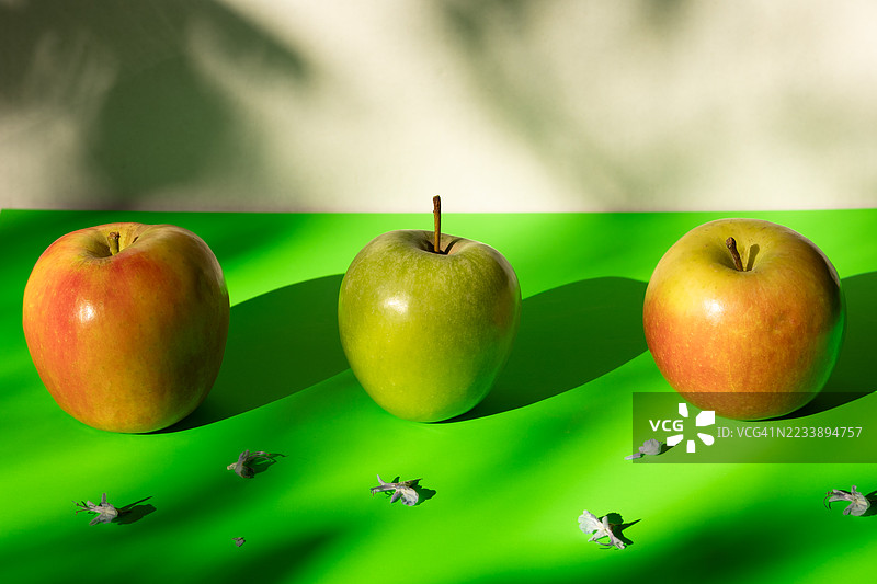 三只苹果放在鲜艳的绿色表面上，伴有阴影。图片素材