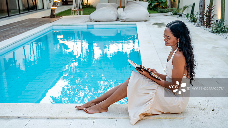 女人在宁静的泳池边阅读一本书图片素材