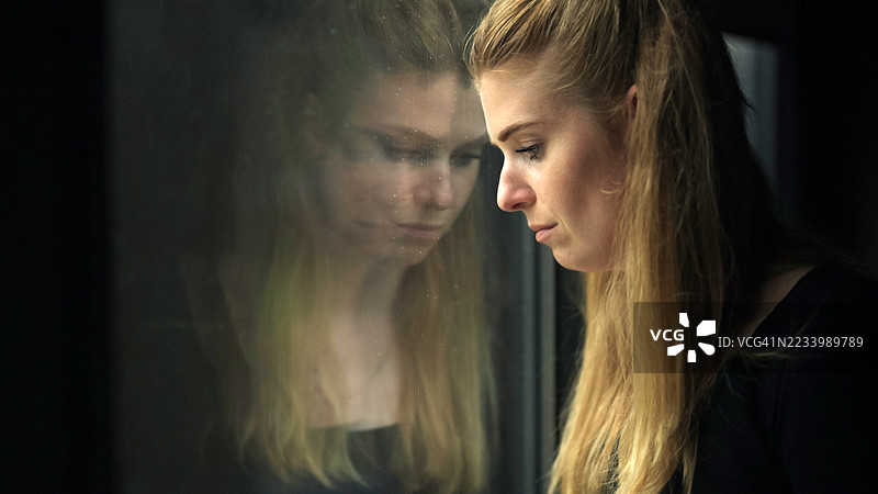 一个抑郁的女人。她的脸映在窗户玻璃上。图片素材