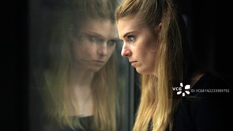 一位抑郁的女性，她的脸映在窗户玻璃上。图片素材