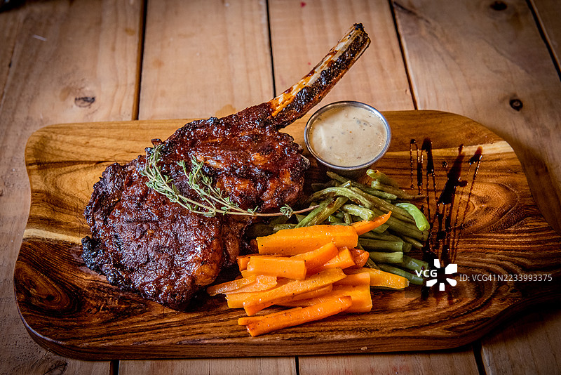 带骨肋眼牛排配蔬菜，放在木质餐盘上图片素材