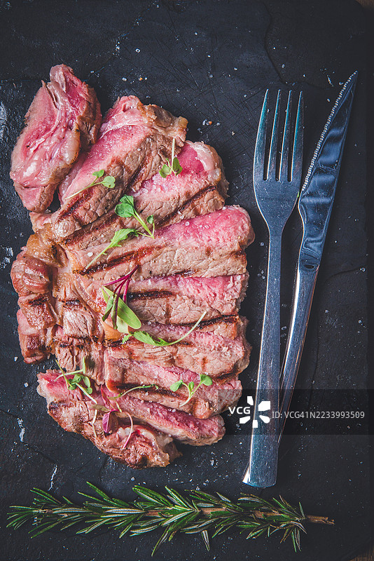 香草烤牛排切片与餐具放在深色石盘上图片素材