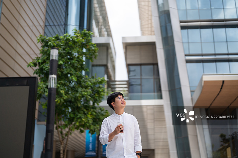 一名穿着白衬衫的男子手里拿着杯子，站在一栋建筑前。图片素材