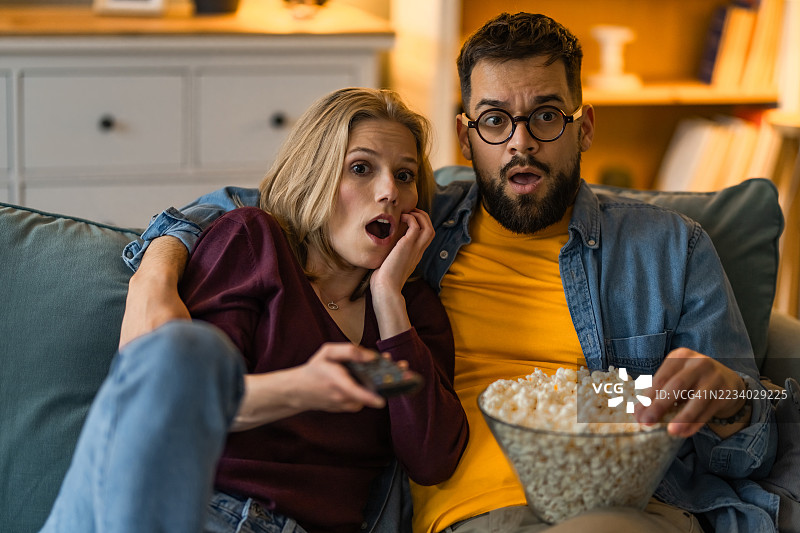 年轻情侣在客厅看恐怖电影，吃着爆米花。图片素材