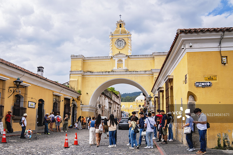 游客在危地马拉安提瓜的圣卡塔利娜拱门下，云层密布的天空下。图片素材