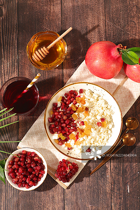 健康早餐配料。柔软颗粒状的奶酪搭配石榴籽、葡萄干、蜂蜜和果汁，摆放在阳光明媚的桌子上，自然食品概念，健康生活方式广告，婴儿食品。图片素材