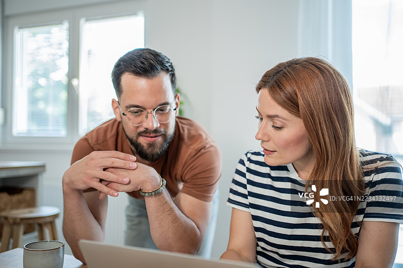 年轻情侣在家工作，一起看着笔记本电脑屏幕。图片素材