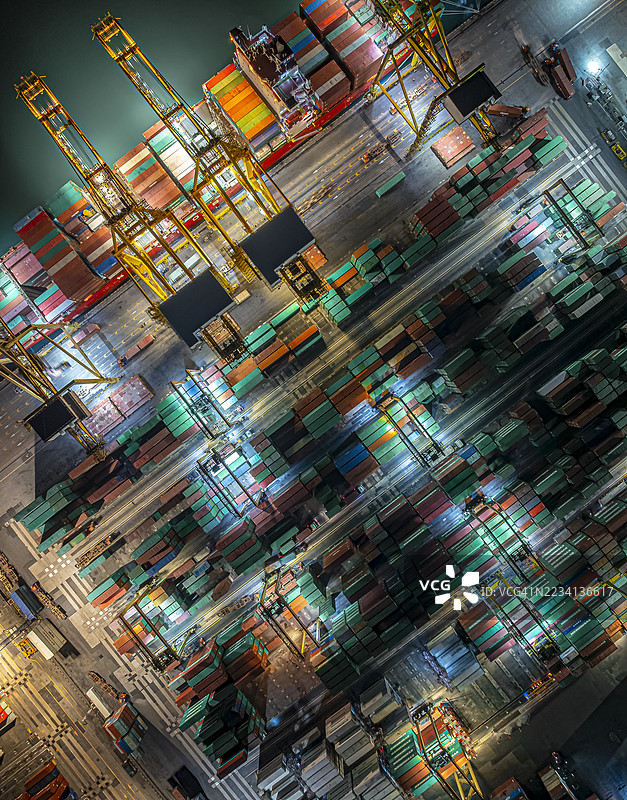 鸟瞰图，起重机在港口夜间将集装箱装载到大型货船上，仓库内的商业贸易物流和运输，进出口集装箱货运船。图片素材