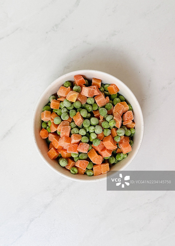 白碗中的冷冻豌豆和胡萝卜，旁边留有空白以便添加文字图片素材