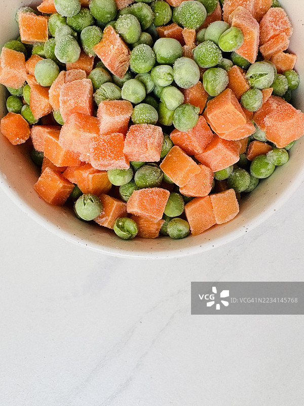 白碗中的冷冻豌豆和胡萝卜，旁边留有空白以便添加文字图片素材