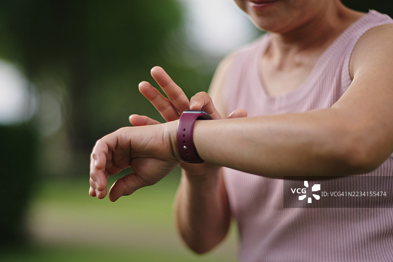 成熟的女性在公园使用智能手表。图片素材