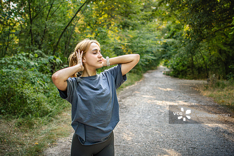 美丽的年轻女性穿着运动服，在大自然中热身或拉伸。她在锻炼过程中平衡力量与柔韧性。积极的生活方式、心理健康与健身。图片素材