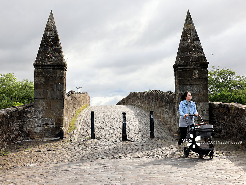 一位女性在苏格兰斯特灵的历史悠久的斯特灵老桥上推着婴儿车。图片素材
