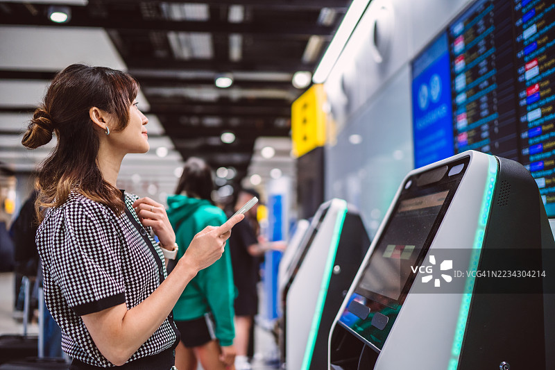 女性在机场航站楼查看航班信息并使用自助服务终端图片素材