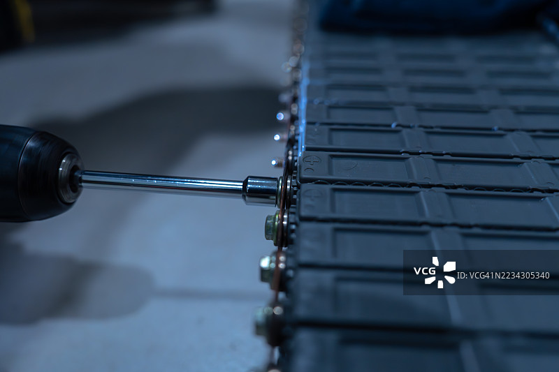 电动汽车电池组装过程的特写，使用电钻。通过先进的技术解决方案提升汽车效率。图片素材