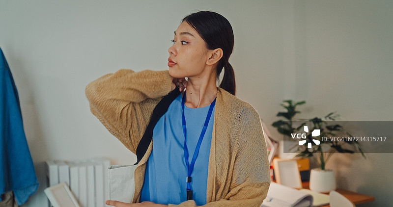 年轻亚洲女性护士在卧室里穿着米色毛衣，身穿蓝色护士服的特写。护士生活方式概念。图片素材