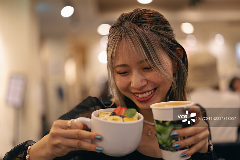 快乐的年轻女性在咖啡馆里手拿水果酸奶和咖啡图片素材