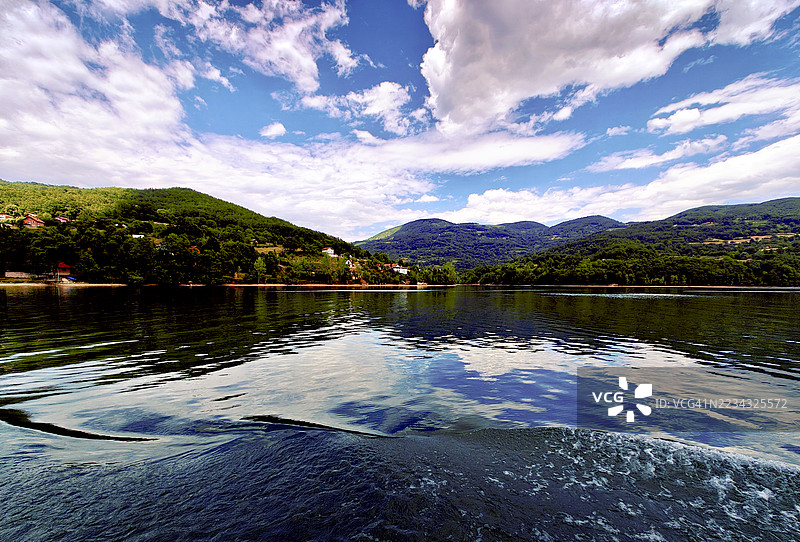 宁静的湖泊被郁郁葱葱的绿色山丘环绕，天空多云，斯雷布雷尼察，波斯尼亚和黑塞哥维那图片素材