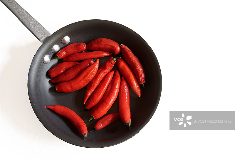 一口装满鲜红辣椒的黑色平底锅，背景为白色。图片素材