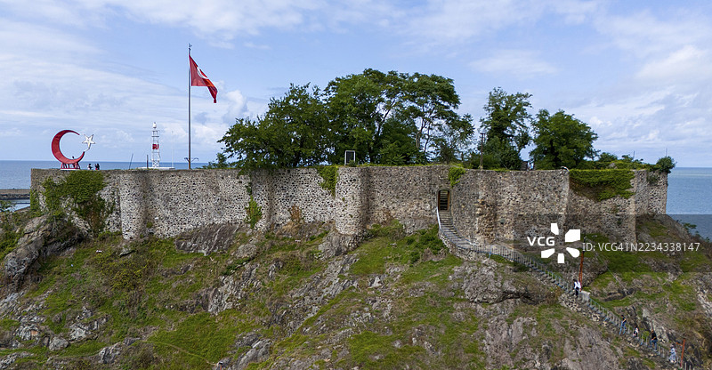 从空中俯瞰,一座插着旗帜的城堡坐落在岩石上,周围环绕着自然风光,这是一座要塞,位于土耳其黑海吉雷松省的特里波利。图片素材