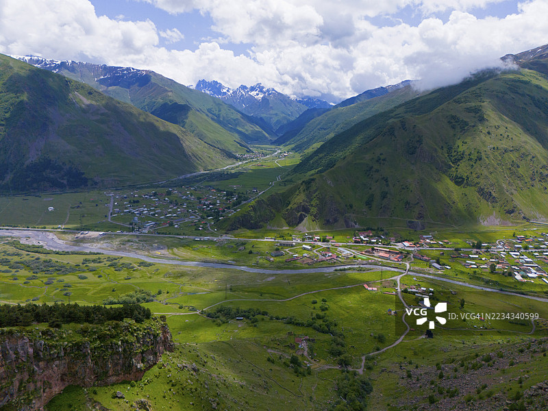 绿色山谷,河流与村庄,四周环绕着高山和多云的天空,鸟瞰图,俯瞰Snostskali河和Terel河的山谷,托提,卡兹别吉,卡斯别吉,斯捷潘茨敏达,格鲁吉亚军事公路,姆茨赫塔-姆季安尼省,希格图片素材
