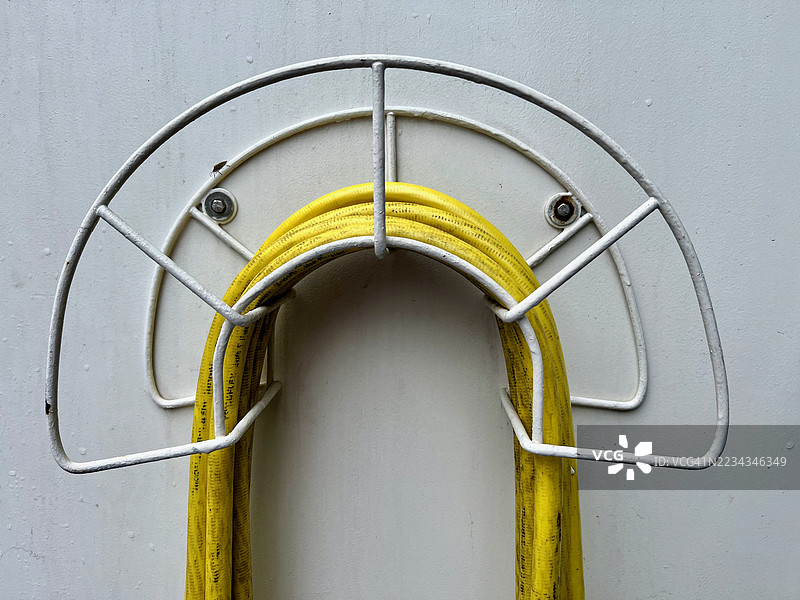 黄色水管盘绕在白色金属支架上，靠在墙壁上图片素材