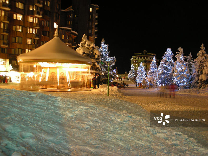 夜间冬季场景，旋转木马与被雪覆盖的树木，法国阿沃里亚兹图片素材