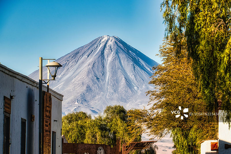 智利圣佩德罗·德·阿塔卡马，远眺宏伟的利坎卡布尔火山，树木与建筑构成画框图片素材