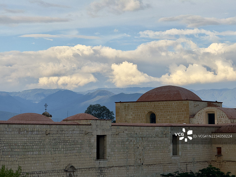 墨西哥瓦哈卡的历史石建筑与多云的山脉天空下的圆顶图片素材