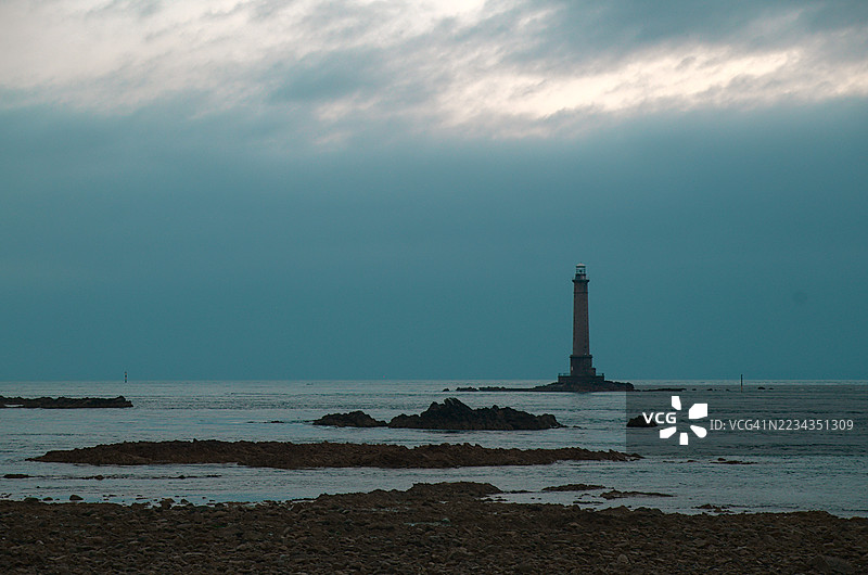 法国岩石海岸上的灯塔在多云的天空下图片素材