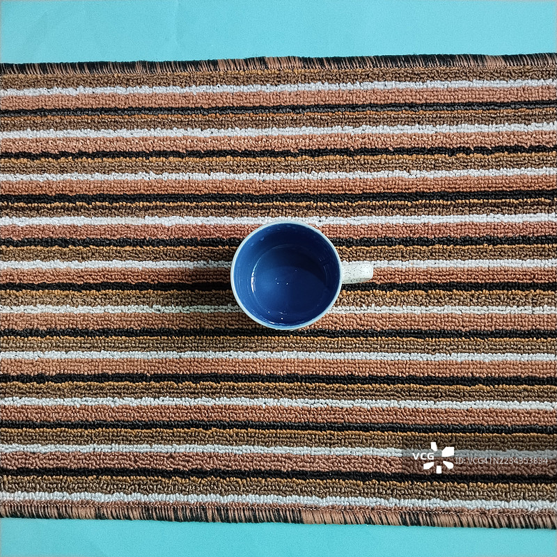 从上方俯视一只蓝色杯子放在条纹地毯上图片素材